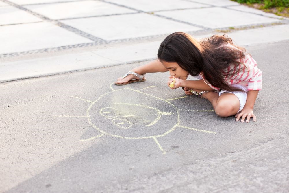 Flicka ritar på gatan i solen